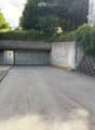 A concrete garage entrance with a raised ground floor, surrounded by greenery and a stone wall.