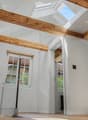 Bright, airy hallway with exposed wooden beams, skylights, and a staircase leading upwards. White walls and wooden flooring.