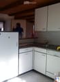 modern kitchen with white tiles, cabinets, countertop, sink, dishwasher, bottles, yellow sponge, wooden beam