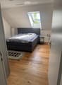 Modern bedroom with wooden flooring, a large bed with dark headboard, nightstand, and a patterned rug.
