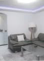 Modern living room with a grey sectional sofa, white throw pillows, a glass coffee table, a floor lamp, and a small white cabinet in the background.
