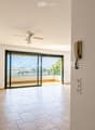Empty hallway with tiled floor, white walls, ceiling fan, and large sliding glass door leading to a balcony with a scenic view.