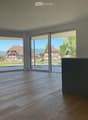 Empty room with wooden flooring, large sliding glass doors leading to a view of a suburban neighborhood, and a small kitchen counter with a faucet visible on the right side.