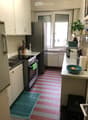 A compact kitchen with white cabinets, stainless steel appliances, and a striped red and white tiled floor. Features include a refrigerator, oven, sink, and various kitchen items on the counter.