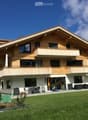 Two-story house with wooden balconies, large windows, and a well-maintained lawn.