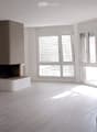 Empty room with wooden flooring, white walls, large windows with blinds, and a fireplace in the center.