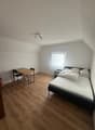 Bedroom with wooden flooring, a bed with white bedding, a nightstand, a small table, and chairs.