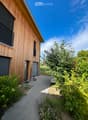 A modern wooden house with a pathway leading to the entrance, surrounded by lush greenery and plants.