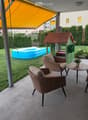 Balcony with wicker furniture, including a sofa, chairs, and small tables, with a view of a backyard featuring a playhouse, inflatable pool, and greenery.