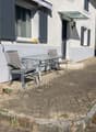 Outdoor seating area with a metal table and four chairs, situated next to a building with shutters and a small awning.