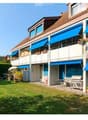 A multi-story residential building with blue awnings, balconies, and a well-maintained lawn in front.
