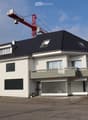 Two-story modern house with white exterior, dark roof, multiple windows, and a balcony on the upper floor.