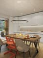 Modern kitchen with white cabinets, a wooden dining table, and a pendant light. The table is set with plates, cups, and a book, and there are chairs around it. An oven is visible in the background, and the space has large windows with a view of the outdoo