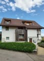 2 story house, white walls, brown roof, wooden balcony, garden, driveway