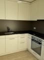 modern white kitchen with black countertops, silver sink, faucet, modern white cabinetry, oven, stove