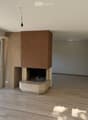 Empty room with wooden flooring, white walls, large glass doors, and a built-in fireplace with a stone base and wooden mantel.