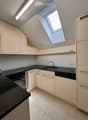 Modern kitchen with white cabinets, black countertops, and built-in appliances including a sink, oven, and dishwasher. Features a skylight window and sleek design.