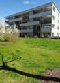 Modern multi-story residential building with balconies, surrounded by a well-maintained lawn and small garden area.