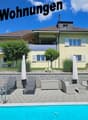 Yellow house, brick wall, blue pool, patio with lounge chairs and tables, fence, trees and plants