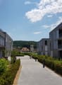 Modern residential complex with grey facades, balconies, and a landscaped courtyard with pathways and greenery.