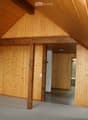 Empty attic space with wooden walls, exposed wooden beams, and a carpeted floor. No furniture or equipment is present.