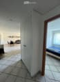 A hallway leads to a furnished room with a bed, a dining area with a table and chairs, and a small cabinet.