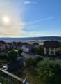 Balcony overlooking a small town with houses, a road, and distant hills under a clear sky.