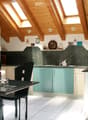Wooden ceiling, wooden floor, green cupboards, white kitchen table, black chairs, countertop, kitchen appliances, wall mounted lamps