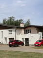 Two-story house with white siding, brown roof, garage, and two parked cars.