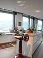 Modern kitchen with large windows offering a scenic view, featuring a kitchen island, cabinets, a sink, a stool, a chair, and a framed picture on the wall.