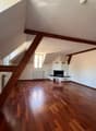 Empty room with wooden flooring, white walls, and a fireplace. Natural light from skylights and windows.