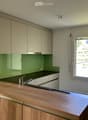Modern kitchen with light-colored cabinets, green backsplash, wooden countertop, and stainless steel sink.
