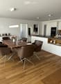Furnished Room. Modern dining area with wooden table, brown chairs, and a white cabinet. A plant and flowers add a touch of nature. The kitchen has a counter, microwave, and oven.