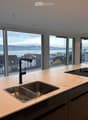 Modern kitchen with a marble countertop, stainless steel sink, black faucet, and induction cooktop, large windows offering a scenic view of the city and water.