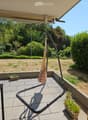 Balcony with tiled floor, metal railing, hanging striped bag, potted plants, and a view of a landscaped garden.