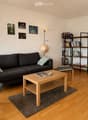 Modern living room with wooden flooring, grey sofa, wooden coffee table, armchair, bookshelf, and decorative picture frames on the wall.