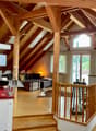 Open-plan attic space with exposed wooden beams, high ceilings, and skylights. Features a living area with a sofa, coffee table, and decorative items, a kitchen area with a red countertop, and a staircase leading to another level.