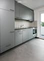 Modern kitchen with dark gray cabinets, light gray countertops, silver sink, stainless steel faucet, large windows, balcony