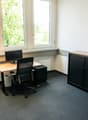 Office space with a desk, chair, computer monitor, cabinet, round table, and floor lamp. Large windows provide natural light.