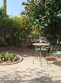 A small outdoor patio with a round table and two chairs, surrounded by lush greenery and plants.
