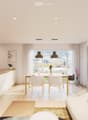 Open-plan living and dining area with modern furniture, large windows, and a kitchen island. Features a sofa, coffee table, dining table with chairs, and a kitchen area with a sink and countertop.