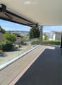 Modern balcony with wooden decking, glass railing, and scenic view of surrounding houses and landscape.