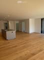 Empty room with wooden flooring, white walls, and large sliding glass doors leading to a balcony. Minimalist design with recessed lighting.