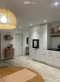 Modern kitchen with white cabinets, a round wooden dining table, a coffee maker, and a large hanging light fixture.