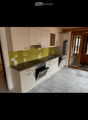 Modern kitchen with light-colored cabinets, granite countertop, stainless steel appliances, and a green backsplash.