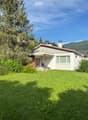Single-story house with a sloped roof, surrounded by a well-maintained lawn and trees, with a scenic mountain view in the background.