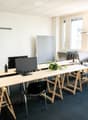 Modern office space with multiple desks, chairs, computer screens, keyboards, and a small plant on one of the desks.