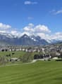 Scenic view of a town nestled in a valley surrounded by mountains, with green fields and scattered buildings.