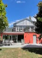 Modern orange house with a large balcony and outdoor dining area, surrounded by greenery and trees.