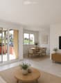 Bright living and dining area with white walls, tiled floor, large sliding glass doors leading to a balcony, sofa, coffee table, TV, dining table, and chairs.